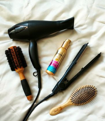 Flat lay of hair styling tools with Pantene heat&glow leave in cream product on a white silk background.